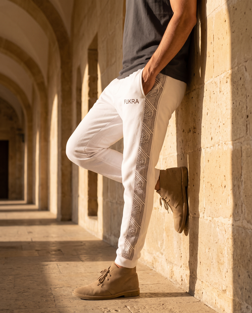 Geometry Joggers in bone white, leaning on a limestone wall at golden hour